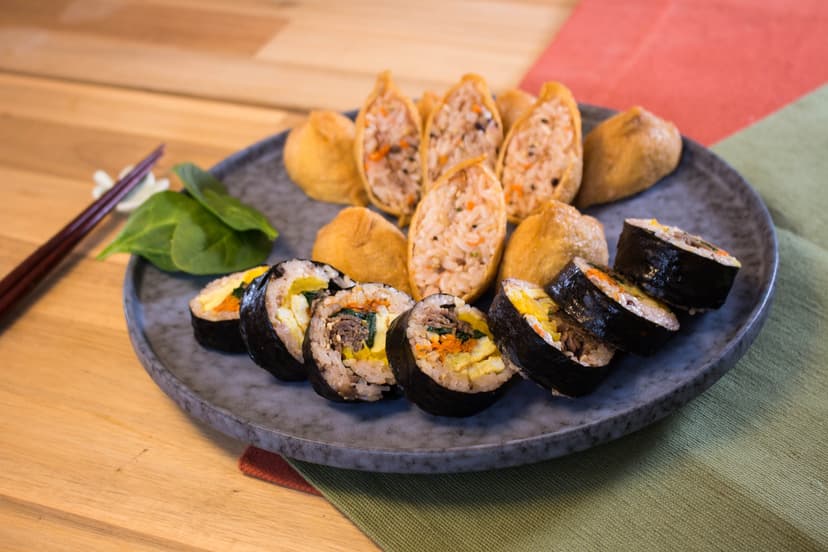 Kimbap and inari sushi platter with chopsticks on wooden table