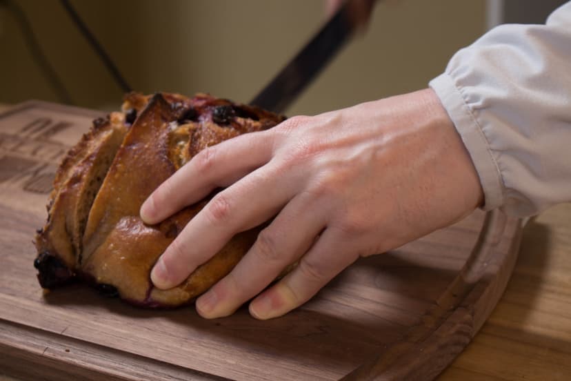 Hand slicing blueberry bread on a wooden cutting board