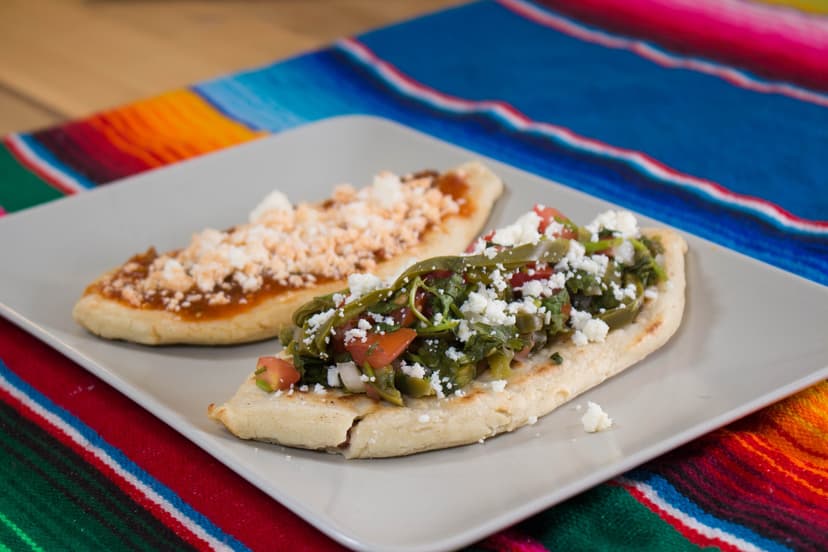 Mexican tlacoyos topped with nopales and queso fresco on a colorful serape